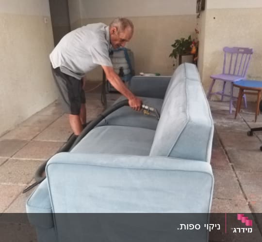 אדם מנקה ספה עם שואב אבק ידני